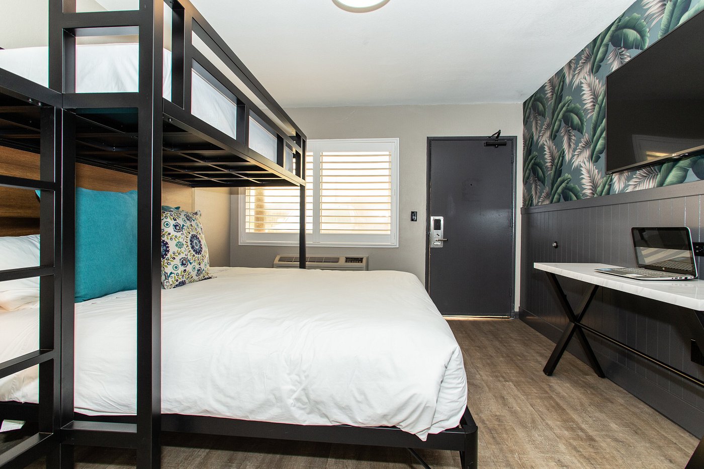 A hotel room with bunk beds, a desk, and a TV on the wall.