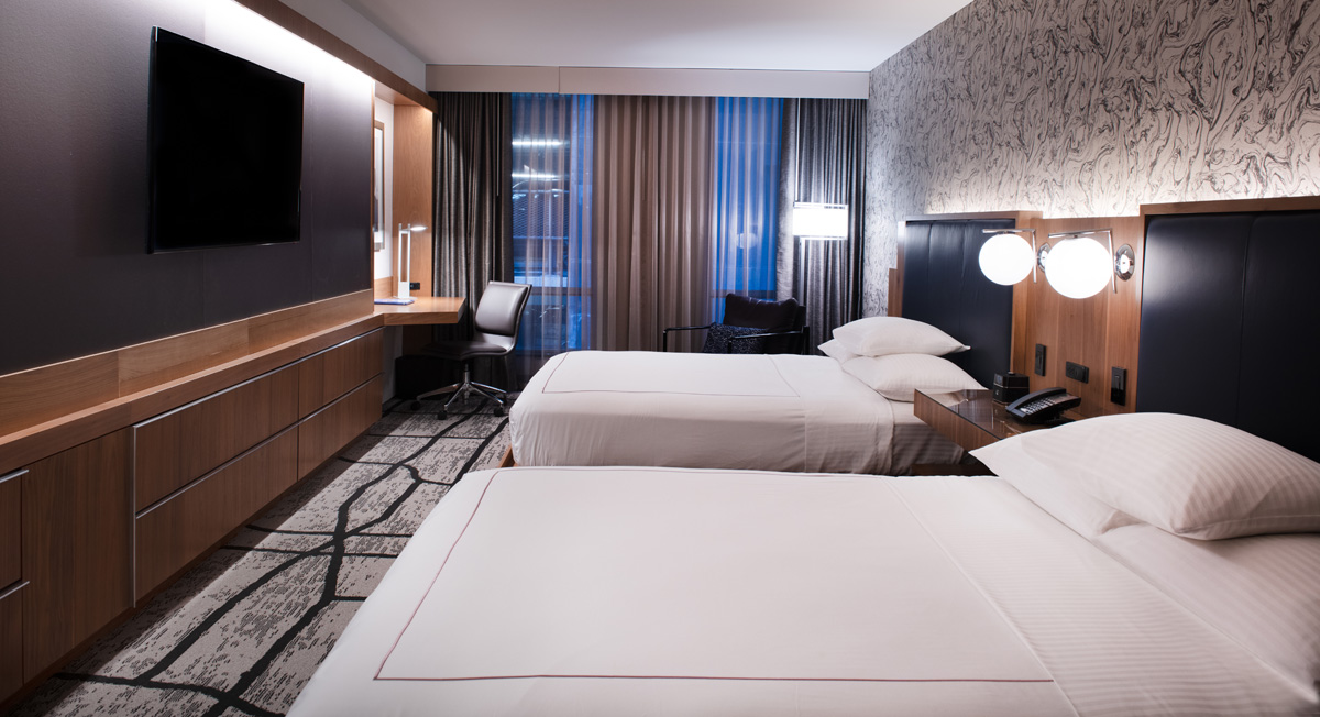 A hotel room with two beds, a desk, and a window.