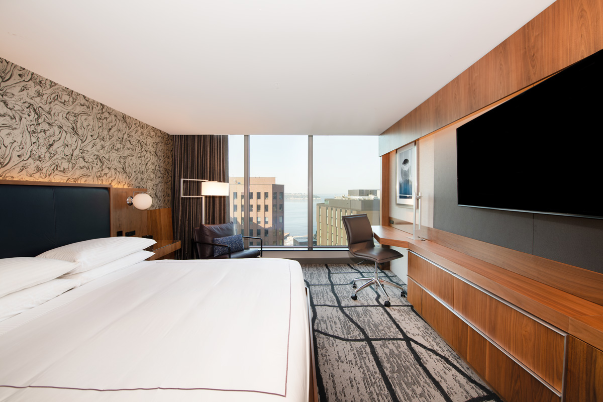 A hotel room with a large bed, TV, desk, and window
